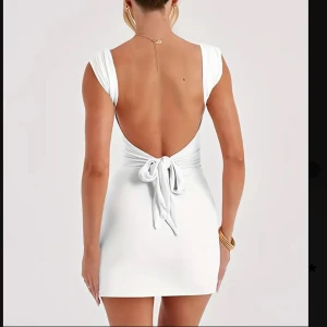 Vit kortklänning med öppen rygg - Snygg vit kortklänning med öppen rygg och knytning. Klänningen har en tight passform och är ärmlös med en liten slits på sidan. Perfekt för sommarens fester! Helt ny aldrig använd 🥰🩷