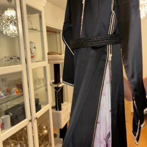 Marockansk bröllopsklänning/festklänning. Svart och blommig klänning med detaljer - Äkta handsydd marockansk takshita ( bröllops/festklänning! Tygen är själv designad av mig och klänningen är broderad av den kända Haute couturen signaturebysamira. Klänningen består av 2 delar. Underdelen till kaftanen är i tyget silkes chiffong. Överdelen är av sidensatin, och till sist kommer ett bälte med svarta pärlor. Klänningen är designad med handgjorda insydda äkta swarowaski stenar vitt som ni kan se på bilder på framsidan,ärmar och kragen fram och bak på den svarta delen. Köpt för 35k