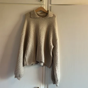 Beige stickad tröja från Uniq Young - Säljer en mysig beige stickad tröja från Uniq Young. Tröjan har en fin krage och ett diskret mönster som ger den en stilren look. Perfekt för kyligare dagar. Passar bra till både jeans och kjol.