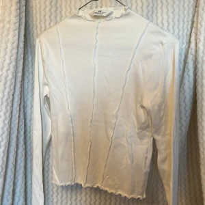 Vit ribbad topp från H&M🤍 - Säljer en stilren vit ribbad topp från H&M med långa ärmar och en fin volangdetalj vid halsen och nederkanten. 🥥