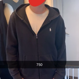 Svart hoodie från Polo Ralph Lauren - Säljer en stilren svart hoodie från Polo Ralph Lauren med dragkedja och det klassiska logotypbroderiet på bröstet. Perfekt för en avslappnad look. Hoodien har långa ärmar och en bekväm passform. 
