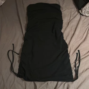 Svart axelbandslös klänning från Miss Selfridge - Snygg svart axelbandslös klänning från Miss Selfridge. Klänningen har en tight passform med snörning på sidorna för en justerbar look. Perfekt för en kväll ute eller en speciell tillställning.