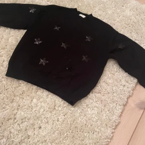 Svart tröja med stjärnor från Gina Tricot - Säljer en svart tröja från Gina Tricot dekorerad med glittriga stjärnor. Tröjan har långa ärmar och en bekväm passform. På bild 1 så ser den smutsig ut men den är inte det i verkligheten. Använd fåtal gånger