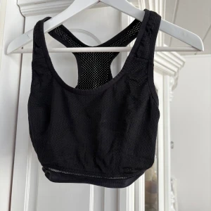 Svart sporttopp från Wear - Säljer en svart sporttopp från Wear med brottarrygg och meshdetaljer för extra ventilation. Perfekt för träning och ger bra stöd. Toppen är i ett stretchigt material som formar sig efter kroppen.