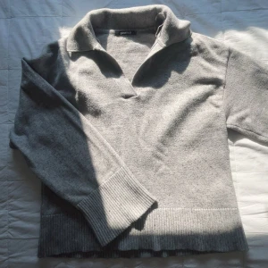 Grå stickad tröja med krage från Gina Tricot - Mysig grå stickad tröja med bred ribbad mudd och krage. Tröjan har lång ärm och en avslappnad passform. Enkel och stilren design som passar till det mesta. 