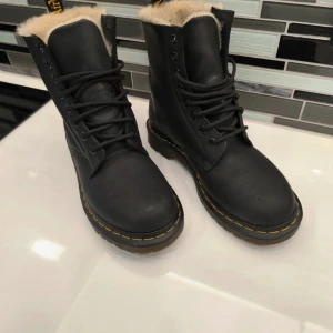 Svarta boots med foder Dr Martens  - Säljer ett par svarta Dr. Martens boots med snörning och varmt foder. De har den klassiska gula sömmen och en robust sula. Perfekta för kyligare dagar.
