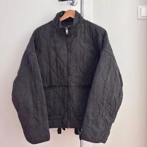 Zara Svart quiltad jacka - Säljer en svart quiltad jacka med dragkedja från Zara. Jackan har en hög krage och långa ärmar. Använd endast en gång.