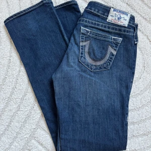 True Religion jeans mörkblå - Jättefina lågmidjade jeans från True Religion med glitterdetaljer på fickorna. Köpta i USA för något år sedan, men fortfarande i bra skick! Byxorna har ett inbyggt snöre i midjan, så de går att justera i midjan. Jeansen är lågmidjade och bootcut!