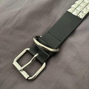 Svart bälte med nitar - Svart nit bälte. Cirka 95cm lång med 7 olika hål som kan anpassa bältets längd. Bältet kan som kortast vara runt 73cm kort. Super bra skick har inte använt bältet så jätte mycket. 