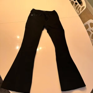 Svarta bootcut jeans från True Religion - Snygga svarta bootcut jeans från True Religion med klassiska femficksdesign och dekorativa sömmar på bakfickorna. Perfekta för en stilren look.