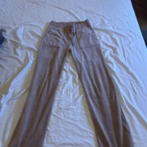 Beige mjukisbyxor från Juicy Couture - Säljer ett par bekväma beige mjukisbyxor från Juicy Couture. Byxorna har en elastisk midja och dragkedja på fickorna för extra stil och funktionalitet. Perfekta för en avslappnad look.