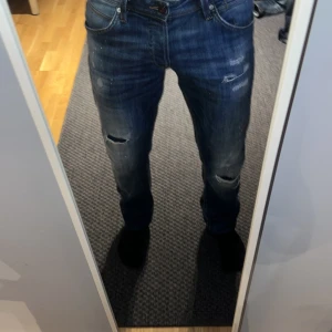 Blå Jack & Jones jeans med slitningar  - Snygga blå jeans med coola slitningar och en lätt tvättad look. De har en klassisk femficksdesign och en knappgylf. Perfekta för en avslappnad stil. Är W30 L34 men sitter som W30 L32. Lägg prisförslag!!!!