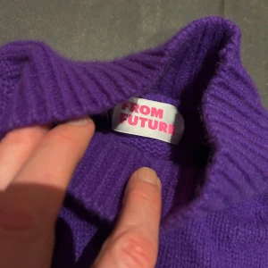 Lila stickad tröja från From Future - Säljer en snygg lila stickad tröja från From Future med texten 'FUTURE' i vitt på framsidan. Tröjan har en ribbad design och en hög krage som ger extra värme. Perfekt för kyliga dagar!