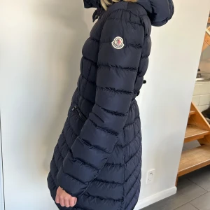 Mörkblå dunjacka från Moncler - Säljer en snygg mörkblå dunjacka från Moncler med huva och dragkedja framtill. Jackan har en quiltad design och långa ärmar. Perfekt för kyliga dagar!