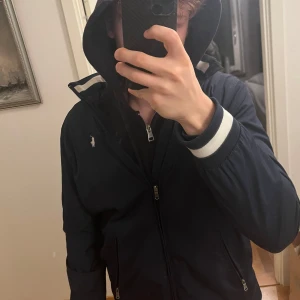 Mörkblå jacka från Ralph Lauren - Mörkblå Windbreaker från Ralph Lauren med justerbar luva(kan vecklas in). Jag är 180 och den sitter lite tajt på mig och på gränsen till lite för kort. Det står att det är XL men skulle säga mer åt S hållet. Skulle säga att perfekta passformen skulle längdmässigt vara 172/177. Pris kan diskuteras och var inte rädd för att ställa frågor vid funderingar. 
