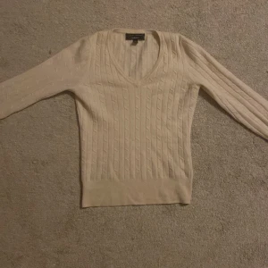 Vit stickad tröja från GANT - Säljer en stilren vit stickad tröja från GANT i lammull. Tröjan har en v-ringad design och långa ärmar med ett klassiskt kabelstickat mönster. Perfekt för kyligare dagar, men passar även i varmare miljö!💕