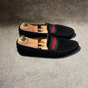 Gucci Loafers  - Hej! Säljer dessa grymt snygga Gucci Loafers med svart mocka kombinerat med de 2 ikoniska färgerna Grön och röd vilket representerar märket! Väldigt fint skick inre och yttre förutom att en liten gummiplupp lossnat längst bak på sulorna (se bild 4) men är inget som känns av eller påverkar användning 😊helt perfekt val till sommaren! Nypris 8000kr+! Mitt pris är endast 1899kr! Box och dustbag medföljs vid köp 🤝skriv vid minsta intresse! Mvh DC 🔹