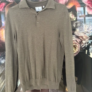 Brun pikétröja från bläck  - Säljer en stilren brun pikétröja från bläck. Tröjan har långa ärmar och en klassisk krage med två knappar. 