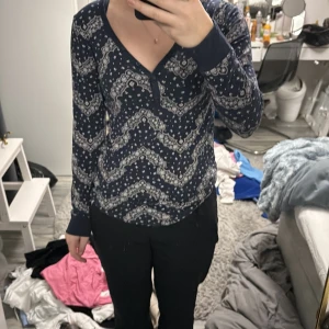 Mönstrad långärmad topp från H&M - Säljer en snygg mörkblå långärmad topp från H&M med ett vitt mönster. Toppen har en v-ringad hals och är perfekt för en stilren look. Passar bra till både jeans och kjol. Perfekt för höst och vår!