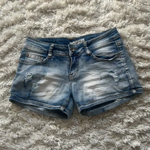 Lågmidjade shorts - Snygga blå jeansshorts med slitna detaljer och klassisk femficksdesign. Perfekta för en avslappnad sommarlook. De har en knapp- och dragkedjestängning framtill.