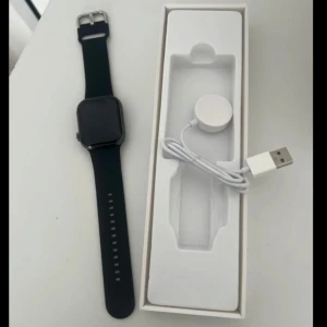 Svart smartklocka med laddare - Säljer en svart smartklocka med fyrkantig skärm och svart armband. Är helt oanvänd. Klockan kommer med en laddare och har så många olika funktioner såsom en apple watch har. Du kan ta bild, ringa, räkna steg, mäta puls osv. Perfekt för den teknikintresserade! Nypris 700kr. Köparen står för frakten 