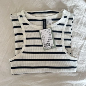 Randig ribbad linnetopp från H&M Divided - Snygg vit och svart randig ribbad linnetopp från H&M Divided. Perfekt för en avslappnad stil med sin ärmlösa design och bekväma passform. Ett måste i garderoben för en stilren look!