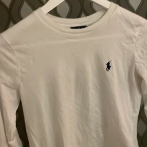 Vit långärmad tröja från Polo Ralph Lauren - Säljer en stilren vit långärmad tröja från Polo Ralph Lauren med det klassiska logotypbroderiet i marinblått på bröstet. .