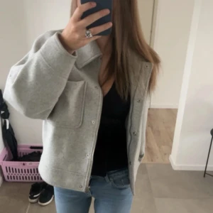 Grå kappa med knappar - Snygg grå kappa med knappar framtill och en stor ficka. Kappan är från NA-KD och har använts flitigt så blivit lite nopprig. Den har även ett pyttelitet hål under kragen men det är inte något som syns. Jag använder noppi på den innan den skickas iväg! Generellt super skick 
