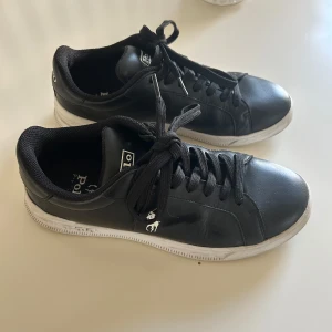 Polo Ralph lauren skor - Snygga svarta sneakers från Polo med klassisk design och vit sula. Skorna har snörning och en rund tå, vilket ger en bekväm passform. Perfekta för en stilren look. Ny pris: 1200. Liten i passform.