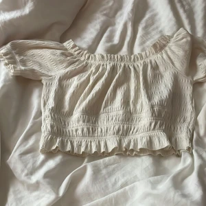 Vit offshoulder topp från Sister - Säljer en söt vit offshoulder topp från Sister i storlek XS. Toppen har en smockad design med volangdetaljer vid ärmslut och nederkant. Perfekt för varma sommardagar! 🌞