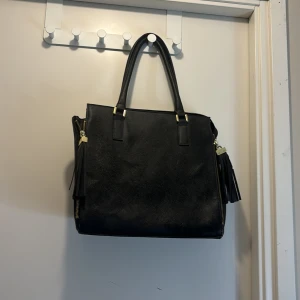 Svart handväska från H&M - Snygg svart handväska från H&M med praktiska dragkedjor och stilrena handtag. Perfekt för att bära med sig det viktigaste. Väskan har en rymlig insida och en elegant design som passar till många tillfällen.