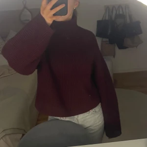 Vinröd stickad tröja från H&M - Säljer en mysig vinröd stickad tröja från H&M. Tröjan har en hög krage och långa ärmar, perfekt för kyliga dagar.