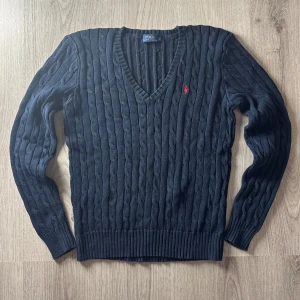 Mörkblå stickad tröja från Ralph Lauren - Säljer en klassisk och stilren Cable Knit-tröja från Ralph Lauren i en djup marinblå färg. Den ikoniska kabelstickningen och den broderade loggan på bröstet gör tröjan tidlös och lätt att matcha till både vardag och finare tillfällen.  🔹 Detaljer: ✔ Modell: Cable Knit Sweater ✔ Färg: Marinblå ✔ Storlek: Large (L) ✔ Material: Mjuk och följsam bomull ✔ Passform: Klassisk – något figurnära ✔ Skick: Ny utan prislapp – aldrig använd  En perfekt tröja nu till hösten!