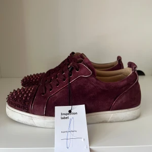 Christian Louboutin Skor - Snygga vinröda sneakers från Christian Louboutin. De är äkta och verifierade som ni kan se på bilderna. Skorna är i väldigt bra skick fast en ni saknas. Skriv vid minsta fundering!