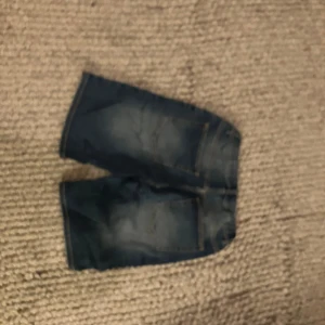 Blå jeansshorts från Lindex - Snygga blå jeansshorts från Lindex med klassisk design och knappstängning. Perfekta för en avslappnad stil under varma dagar.