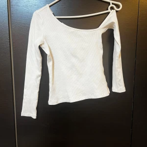 Vit ribbad offshoulder topp - Säljer en stilren vit ribbad topp med offshoulder-design. Toppen har långa ärmar och en bekväm passform som passar perfekt till både jeans och kjol. Perfekt för en avslappnad men chic look.