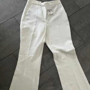 Vita kostymbyxor från Zara - Snygga vita kostymbyxor från Zara med hög midja och raka ben. Perfekta för en stilren look. Byxorna har en klassisk design med dragkedja och knapp framtill. Helt oanvända ordinarie pris 399 kr