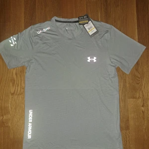 Under Armour tröja - Säljer en grå t-shirt från Under Armour. Aldrig använts förr och skicket är 10/10