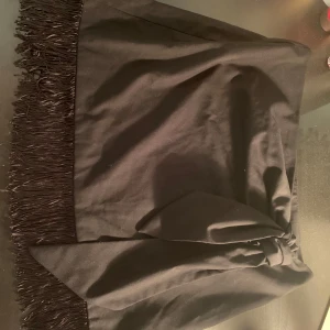 Svart kjol med fransar från Zara - Snygg svart kjol från Zara med fransdetaljer längs nederkanten. Perfekt för att ge en extra touch till din outfit. Tillverkad i ett mjukt material som ger en bekväm passform. Ett måste i garderoben för den stilmedvetna!