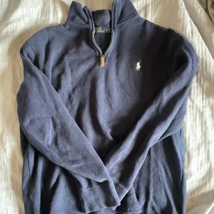 Mörkblå tröja från Ralph Lauren - Säljer en snygg mörkblå tröja från Ralph Lauren med dragkedja och logga på ena sidan bröstet. Använd fåtal tillfällen 