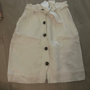 Vit linnekjol med knappar och knytband - Snygg linnekjol med knappar framtill och ett knytband i midjan. Kjolen har en avslappnad passform och är perfekt för varma dagar. ☀️Jättefint skick, rökfritt hem! Skicka meddelande vid frågor/fler bilder 🩷