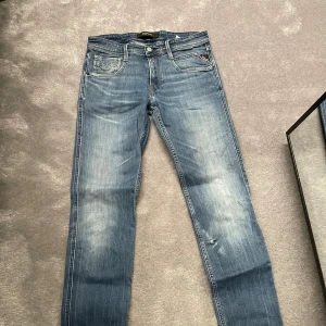 Blå jeans från Replay - Säljer ett par snygga blå jeans från Replay. De har en klassisk femficksdesign och en lätt slitning på framsidan för en trendig look. Perfekta för en avslappnad stil.