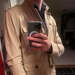 Vintage Beige Overshirt från Moncler - Säljer en stilren vintage beige Overshirt från Moncler med knappar framtill och flera praktiska fickor. Overshirten passar perfekt för vår, sommar och höst, den är långärmad och tillverkad i ett bekvämt material. Extemt gammal model från runt 1995-2005 och därav har den storlek lapp som L. Storleken är mer som M men passar även S. Skriv gärna vid intresse!