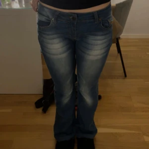 Blå bootcut jeans - Snygga blå bootcut jeans med låg midja och klassisk femficksdesign. Jeansen har en lätt tvättad look med subtila slitningar och är perfekta för en avslappnad stil. Stretchigt material