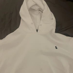 Ralph Lauren Hoodie - Säljer en stilren vit hoodie med en liten broderad logga på bröstet. Den har en klassisk design med huva och dragsko. Perfekt för en avslappnad stil. Passar som S, inga stora defekter! Kom pm för fler bilder, 400kr är sista priset! Storlek XL men passar som M/S
