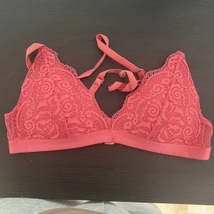 Rosa spets bralette - Säljer en snygg rosa spets bralette med justerbara axelband och hakknäppning bak. Den har ett vackert blommigt spetsmönster och en mjuk resår under bysten för extra komfort. Perfekt för att lägga till en touch av elegans till din outfit.