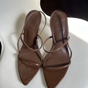 Bruna sandaler med klack - Snygga bruna sandaler med hög klack och spetsig tå. De har en elegant remdesign och är tillverkade i ett glansigt syntetmaterial. Perfekta för att ge en stilfull touch till din outfit.