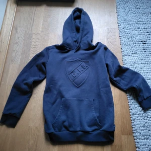 Mörkblå hoodie från Djurgården - Säljer en mörkblå hoodie från Djurgården med ett stort emblem på bröstet som nästan aldrig använts. Den står som 158/164 men passar ännu bättre S (passar dock båda bra). Priset är diskuterbart, så kontakta gärna om du har någon fundering!