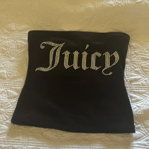 Svart tubtopp från Juicy Couture - Snygg svart tubtopp från Juicy Couture med glittrande text framtill. Perfekt för en stilren och trendig look. Tillverkad i mjukt material för en bekväm passform.