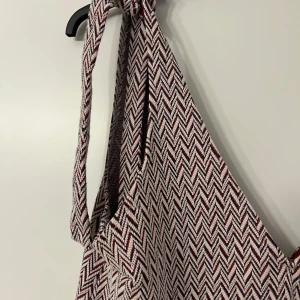 Mönstrad klänning från Pull&Bear - Säljer en snygg klänning från Pull&Bear med ett zigzag-mönster i rött och vitt. Klänningen har en v-ringad design och smala axelband. Perfekt för en stilren look!